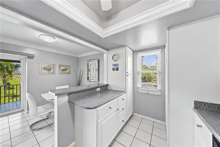 Crisp white cabinetry, a built-in breakfast bar, granite-style countertops, white tile flooring, and a sliding glass door to a balcony