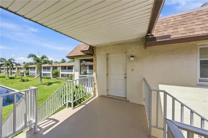 Covered outdoor entryway with white door, stucco exterior, and white railings