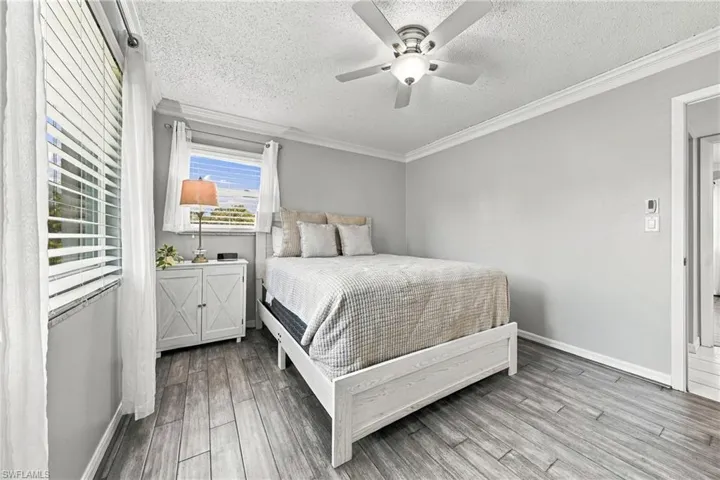 Wood-finish flooring, crown molding, ceiling fan with integrated lighting, and multiple windows with blinds