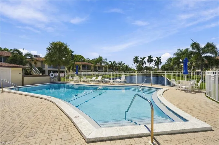 Outdoor swimming pool with integrated steps, surrounded by a paved deck and a white perimeter fence