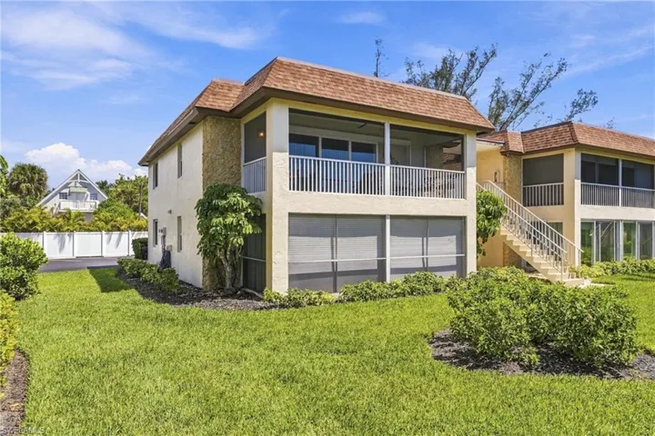 Two-story stucco structure featuring a screened balcony, screened patio, side-facing exterior staircase, and mature landscaping