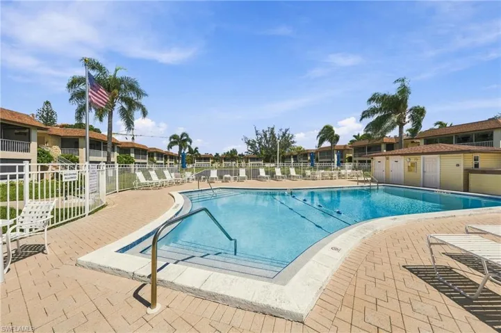 Expansive swimming pool area with paver decking, surrounding white fencing, and tropical landscaping