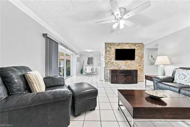 White tile flooring, crown molding, ceiling fan, stone accent wall, and sliding glass door