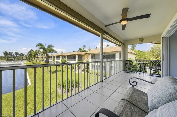 Screened balcony with ceiling fan, tile flooring, and metal railings overlooking a water feature and green space