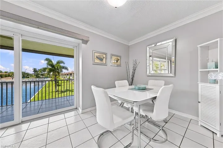 Sliding glass doors opening to a balcony, water feature with lush landscaping, crown molding, tile flooring, and a built-in display cabinet