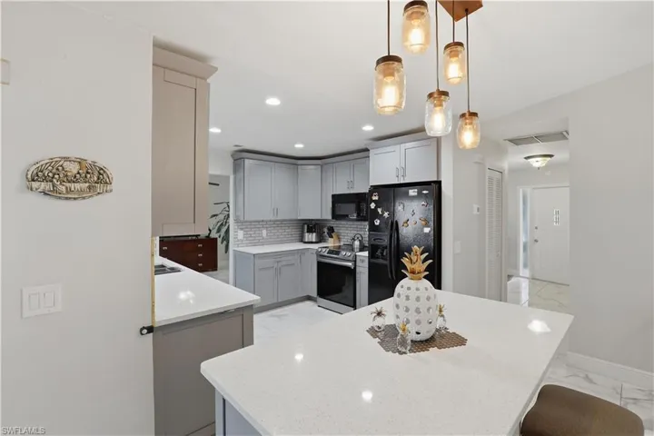 Kitchen with black appliances, gray cabinets, pendant lighting, light stone counters, and light marble finish floors