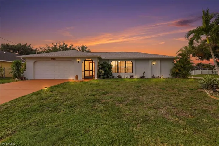View of front of property featuring an attached garage, stucco siding, driveway, and a front yard