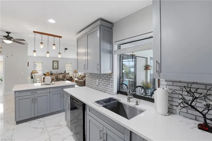 Kitchen featuring gray cabinetry, open floor plan, hanging light fixtures, light stone counters, and decorative backsplash