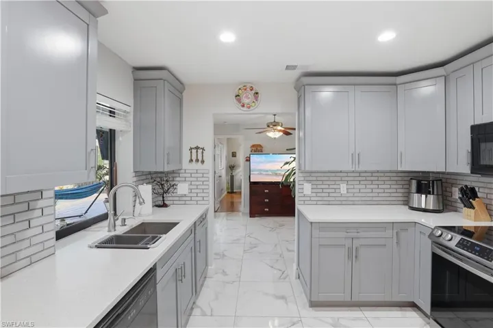 Kitchen with gray cabinetry, black appliances, light marble finish floors, tasteful backsplash, and light stone counters