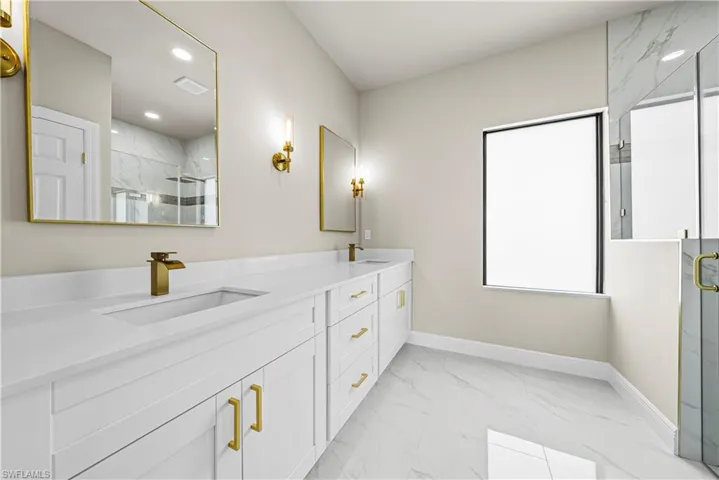 Bathroom featuring a marble finish shower, light marble finish flooring, and double vanity