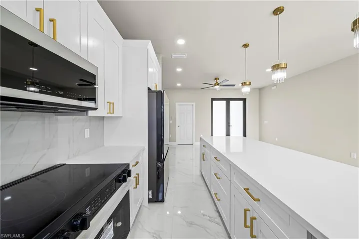 Kitchen with stainless steel microwave, electric range, freestanding refrigerator, white cabinetry, and decorative light fixtures