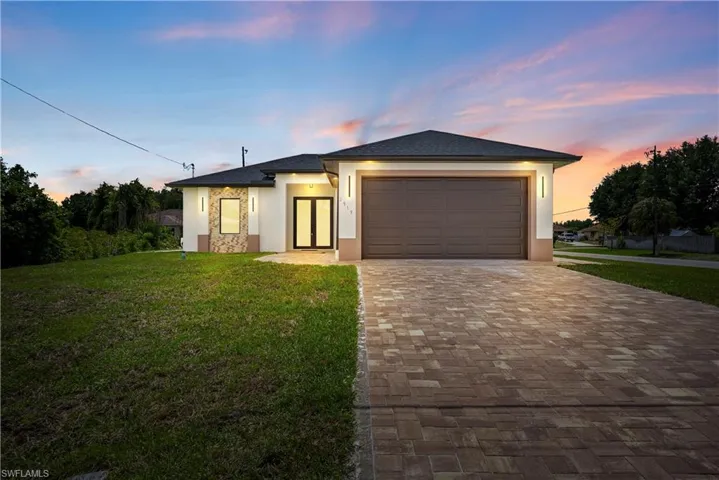 Prairie-style house with a lawn, stucco siding, decorative driveway, and an attached garage