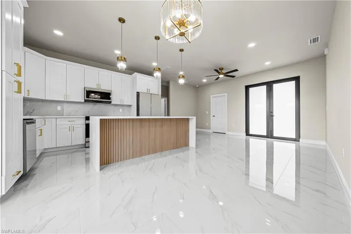 Kitchen featuring a kitchen island, a chandelier, ceiling fan, white cabinetry, and stainless steel appliances