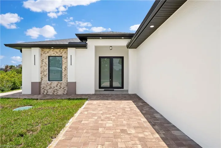 Entrance to property featuring stucco siding, french doors, stone siding, and a yard