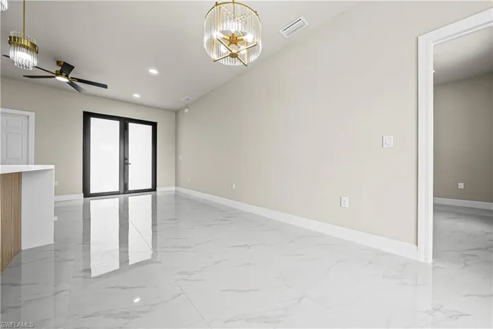 Unfurnished room with a ceiling fan, a chandelier, light marble finish flooring, and french doors