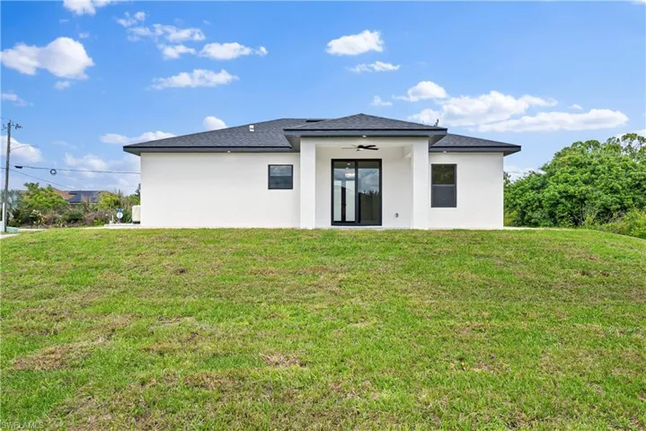 Back of property featuring stucco siding, a yard, ceiling fan, and a shingled roof