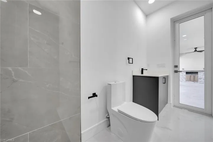Bathroom with vanity, marble finish floor, toilet, baseboards, and a ceiling fan