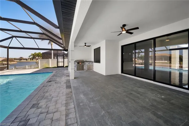 Pool featuring a patio, a ceiling fan, glass enclosure, and exterior kitchen