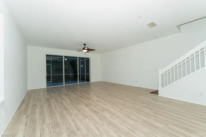 Unfurnished living room featuring light wood finished floors, ceiling fan, and stairs
