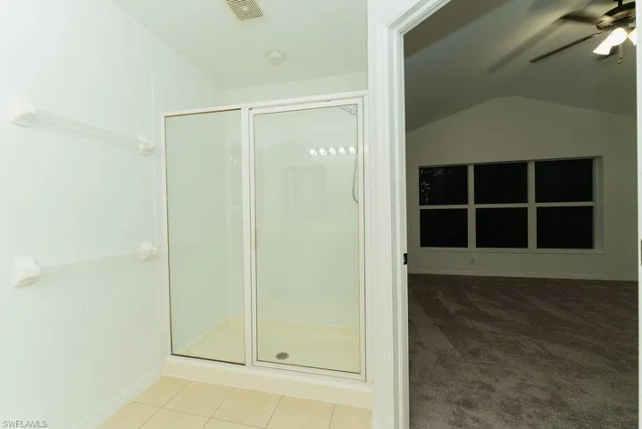 Bathroom featuring a stall shower, ceiling fan, light tile patterned floors, light carpet, and vaulted ceiling