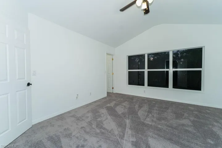 Carpeted empty room with vaulted ceiling and ceiling fan