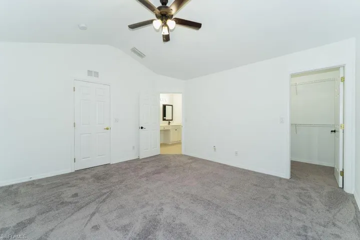 Unfurnished bedroom with lofted ceiling, a walk in closet, carpet flooring, a ceiling fan, and ensuite bath
