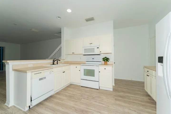Kitchen featuring white appliances, a peninsula, light wood finished floors, light countertops, and recessed lighting
