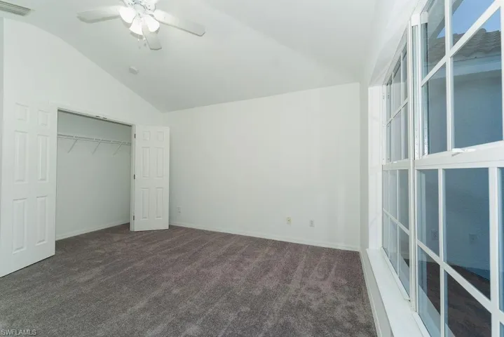 Unfurnished bedroom with dark colored carpet, vaulted ceiling, a closet, and a ceiling fan