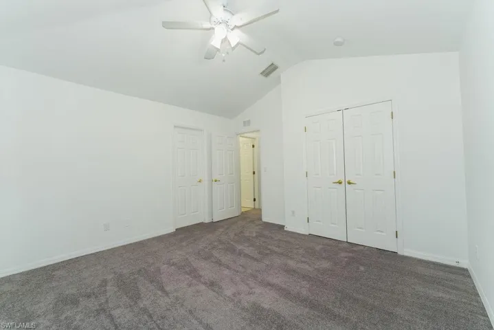 Unfurnished bedroom with carpet floors, lofted ceiling, a closet, and a ceiling fan