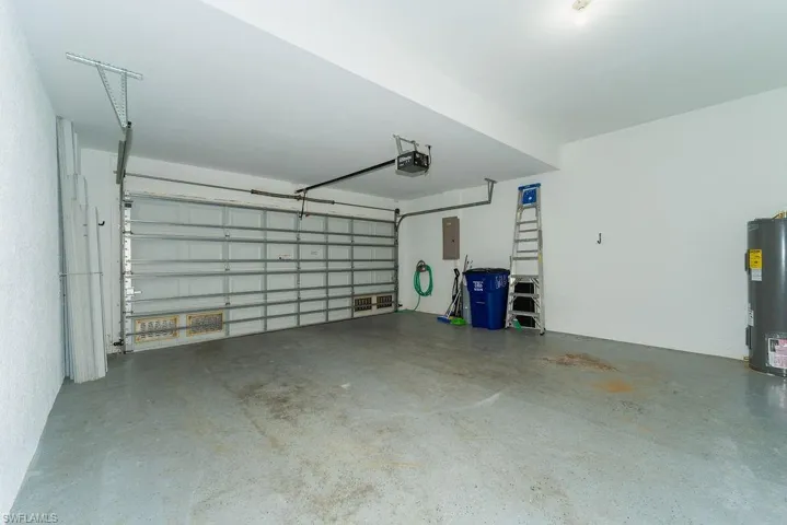 Garage featuring electric water heater, electric panel, and a garage door opener