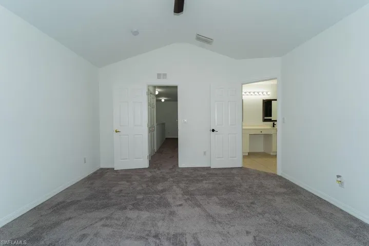 Unfurnished bedroom with carpet, vaulted ceiling, a ceiling fan, and ensuite bath