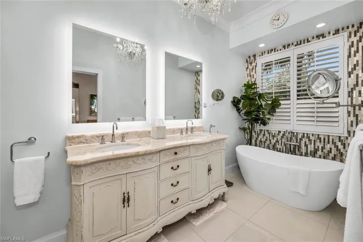 Bathroom featuring a bath, tile flooring, dual bowl vanity, tile walls, and a notable chandelier
