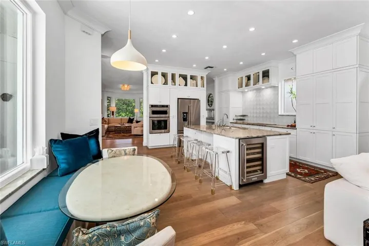 Kitchen with beverage cooler, tasteful backsplash, white cabinetry, an island with sink, and appliances with stainless steel finishes