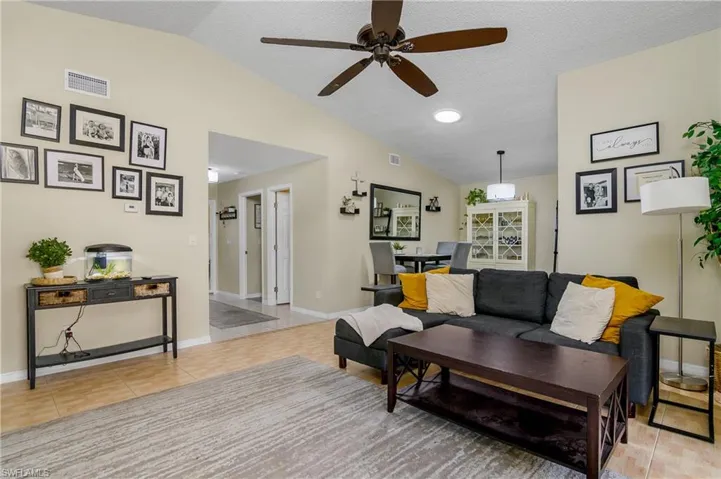 Living room featuring lofted ceiling, ceiling fan, light tile patterned floors, and a textured ceiling