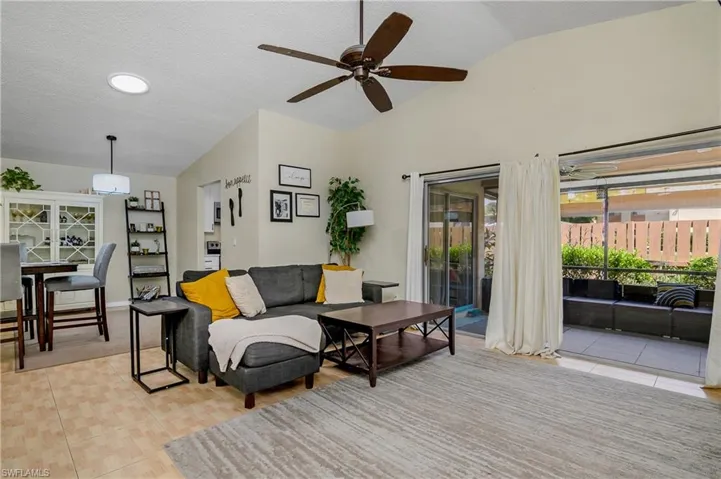 Living room with lofted ceiling, ceiling fan, light tile patterned flooring, and a textured ceiling
