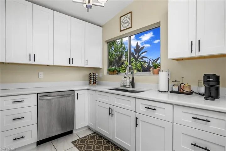 Kitchen with white cabinets, dishwasher, vaulted ceiling, sink, and a textured ceiling