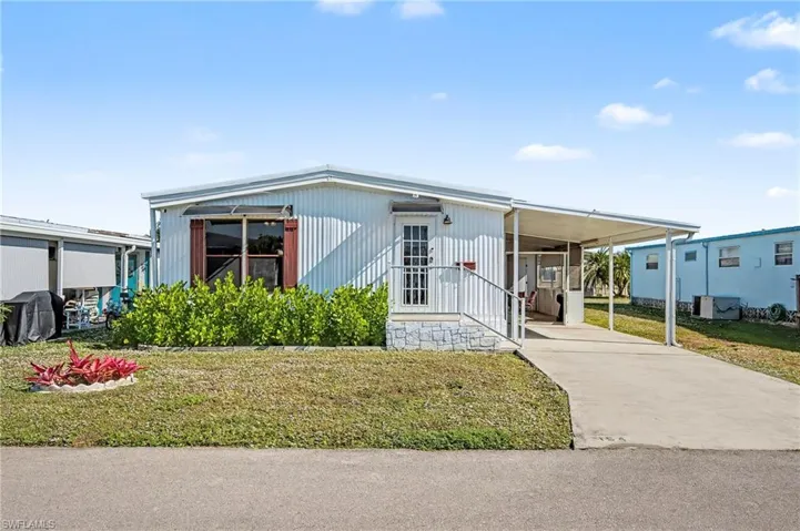 Manufactured / mobile home featuring a front yard, driveway, and a carport
