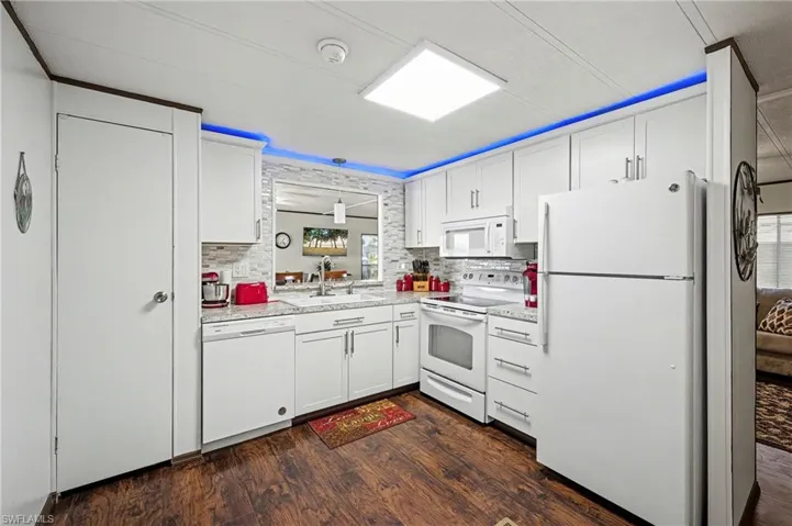 Kitchen featuring white appliances, white cabinetry, dark wood-style flooring, light countertops, and decorative backsplash