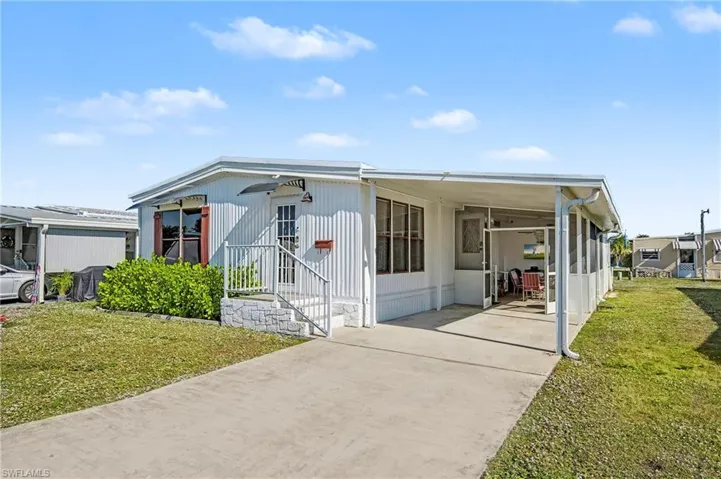 Manufactured / mobile home featuring a front lawn, a carport, and concrete driveway