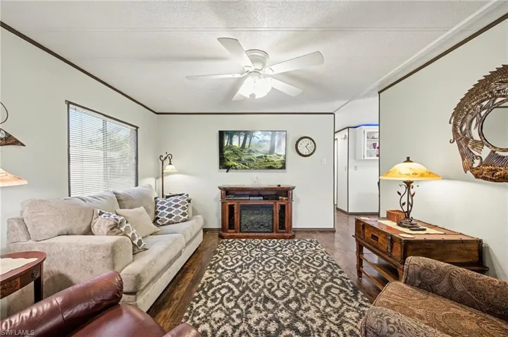 Living area featuring ornamental molding, a ceiling fan, wood finished floors, and a textured ceiling