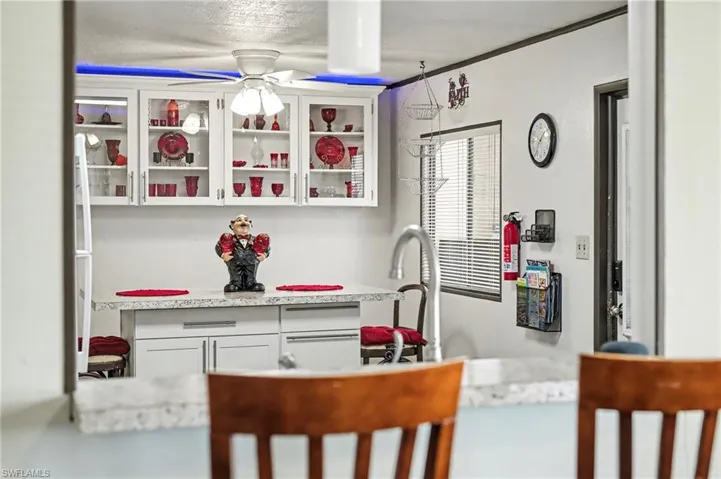Kitchen with white cabinetry, light stone counters, glass insert cabinets, and a ceiling fan