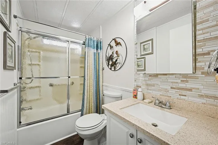 Bathroom with shower / bath combination with glass door, vanity, a textured ceiling, and wainscoting