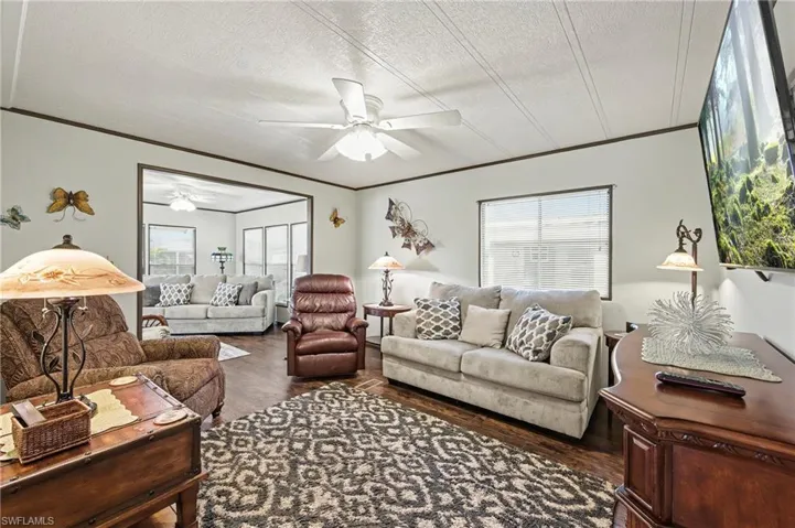 Living room with dark wood-style floors, ornamental molding, ceiling fan, and a textured ceiling