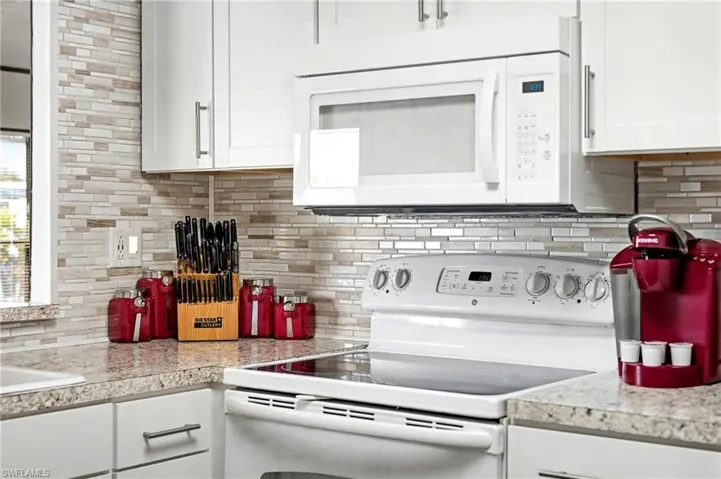 Kitchen featuring white appliances, light countertops, backsplash, and white cabinetry