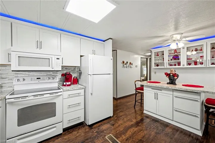 Kitchen with a kitchen breakfast bar, white appliances, white cabinets, and glass insert cabinets