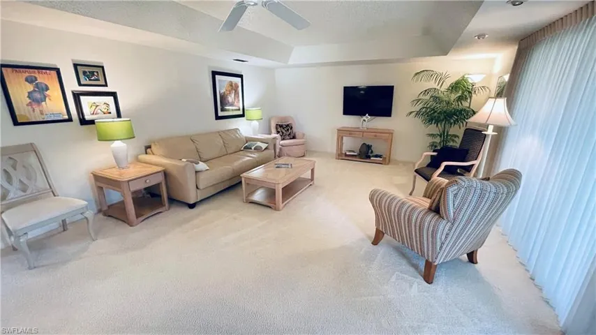 Living room featuring a tray ceiling, light colored carpet, and a ceiling fan