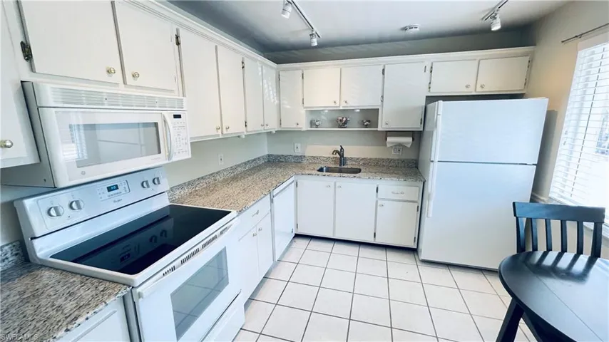 Kitchen featuring white appliances, white cabinetry, rail lighting, open shelves, and light stone countertops