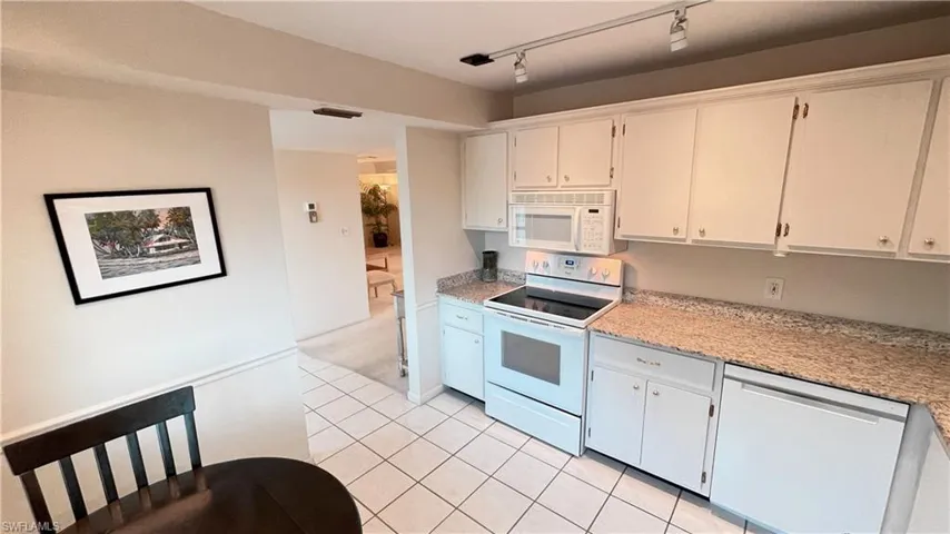 Kitchen featuring white appliances, white cabinetry, rail lighting, light tile patterned floors, and light stone counters