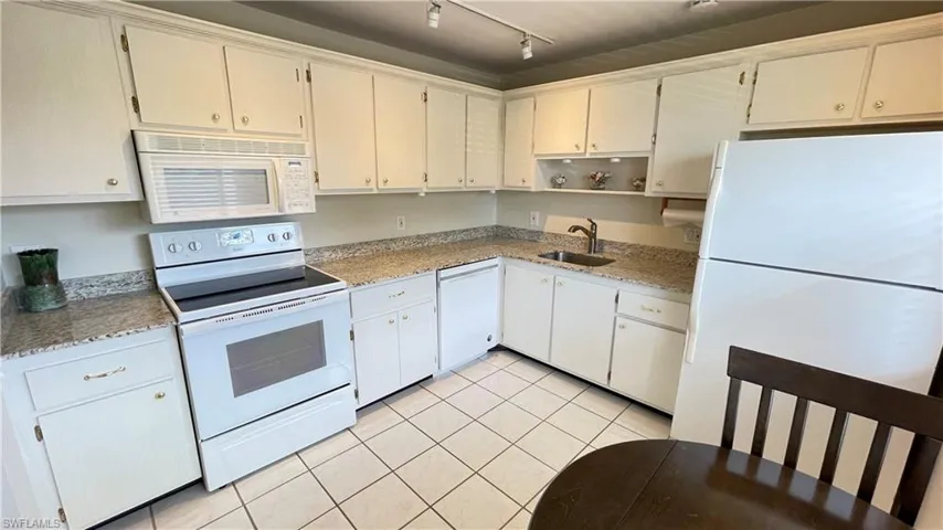 Kitchen with white appliances, light tile patterned flooring, open shelves, light stone countertops, and rail lighting