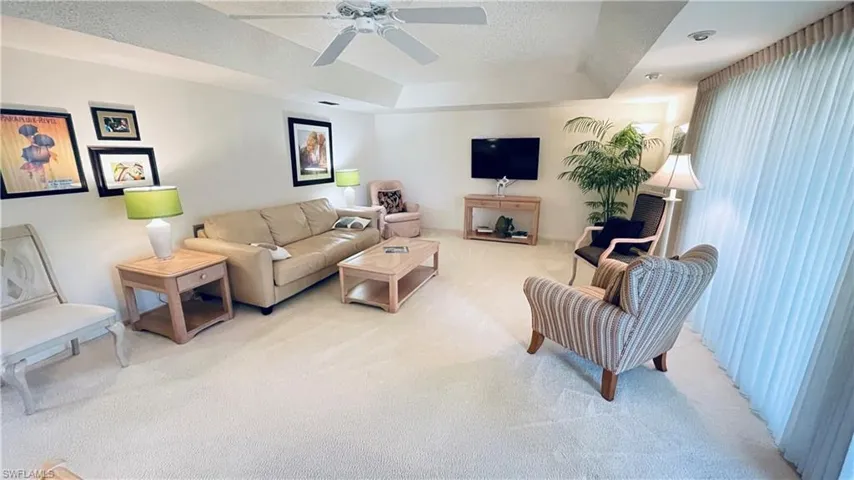 Living room with light colored carpet, a tray ceiling and ceiling fan.